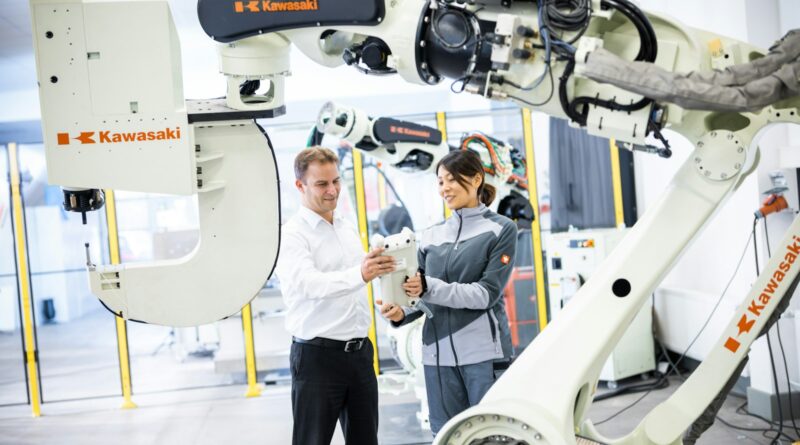 En mand og en kvinde står foran en industrirobot i et værksted